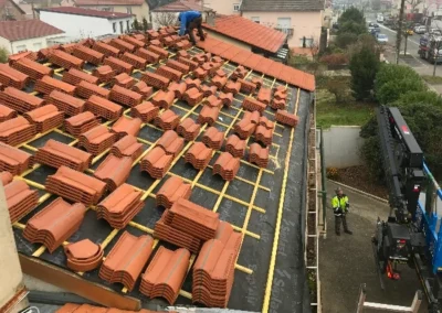 Toiture avec des paquets de tuiles terre cuite r&eacute;partis sur les liteaux et une grue de livraison, couvreurs au travail