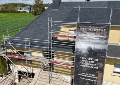 Gros plan sur la b&acirc;che Lux Habitat fix&eacute;e &agrave; l'&eacute;chafaudage listant les services couverture, zinguerie, charpente et r&eacute;parations