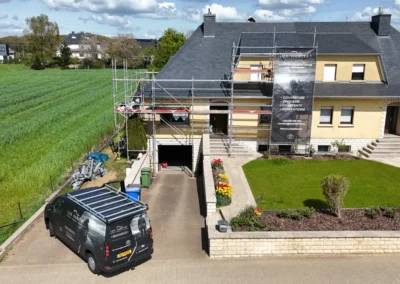 Fa&ccedil;ade d'une maison &eacute;chafaud&eacute;e avec toiture en ardoise et la camionnette Lux Habitat gar&eacute;e dans l'all&eacute;e