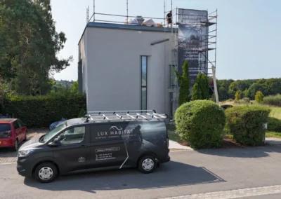 Camionnette Lux Habitat gar&eacute;e devant une maison moderne blanche &eacute;chafaud&eacute;e avec b&acirc;che publicitaire