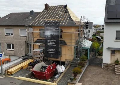 Fa&ccedil;ade d'une maison mitoyenne &eacute;chafaud&eacute;e avec b&acirc;che Lux Habitat, bois de charpente et container de chantier devant