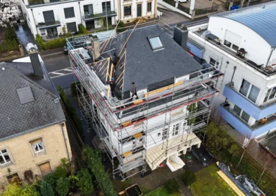 Vue a&eacute;rienne large d'une r&eacute;sidence &eacute;chafaud&eacute;e en cours de r&eacute;novation de toiture, entour&eacute;e de maisons voisines