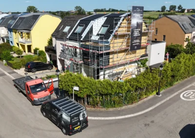 Vue par drone d'un quartier r&eacute;sidentiel avec une maison &eacute;chafaud&eacute;e et les v&eacute;hicules Lux Habitat gar&eacute;s devant
