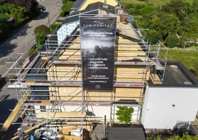 Vue a&eacute;rienne d'un pignon en ossature bois neuve derri&egrave;re un &eacute;chafaudage avec la b&acirc;che publicitaire Lux Habitat