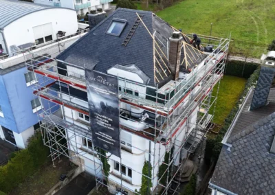 Vue a&eacute;rienne d'une r&eacute;sidence &eacute;chafaud&eacute;e avec couvreurs travaillant au fa&icirc;tage d'une toiture en ardoise