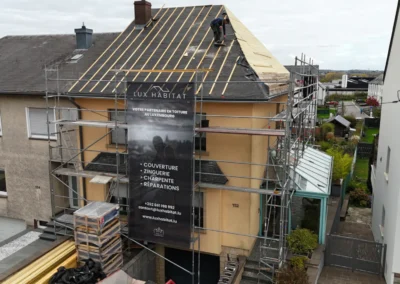 Vue a&eacute;rienne d'une maison mitoyenne &eacute;chafaud&eacute;e dont la toiture est mise &agrave; nu avec un voligeage neuf et des couvreurs au travail
