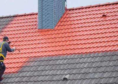 Couvreur appliquant au pulv&eacute;risateur un traitement hydrofuge rouge sur une toiture en tuiles, moiti&eacute; trait&eacute;e