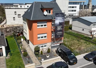 Vue a&eacute;rienne d'une maison orange avec &eacute;chafaudage et b&acirc;che Lux Habitat, camionnette gar&eacute;e devant