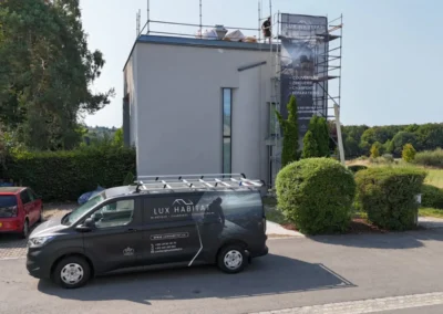 Camionnette Lux Habitat gar&eacute;e devant une maison moderne blanche &eacute;chafaud&eacute;e