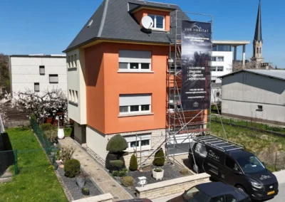 Vue a&eacute;rienne d'une maison orange avec &eacute;chafaudage et b&acirc;che Lux Habitat, camionnette gar&eacute;e devant