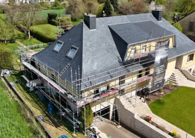 Vue a&eacute;rienne d'une maison avec toiture en ardoise r&eacute;nov&eacute;e, lucarne et fen&ecirc;tres de toit, entour&eacute;e d'&eacute;chafaudages