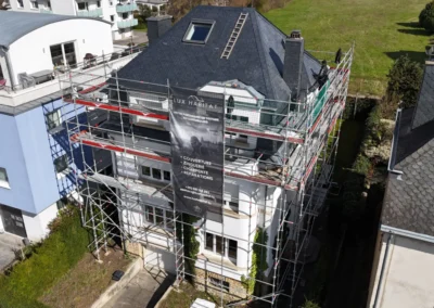 Vue a&eacute;rienne d'une r&eacute;sidence &eacute;chafaud&eacute;e avec toiture en ardoise r&eacute;nov&eacute;e et b&acirc;che Lux Habitat sur la fa&ccedil;ade