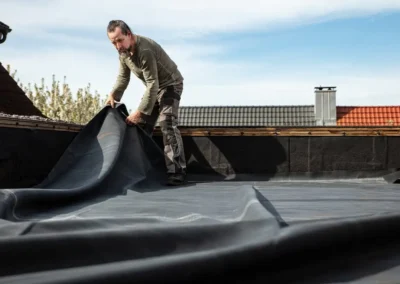 Couvreur d&eacute;roulant une membrane d'&eacute;tanch&eacute;it&eacute; EPDM noire sur un toit plat