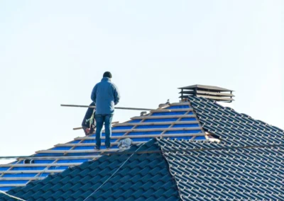Couvreur debout sur une toiture recouverte d'un &eacute;cran de sous-toiture bleu, tuiles en cours de pose