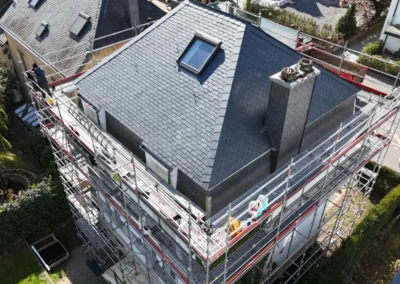 Vue a&eacute;rienne d'un toit en croupe recouvert d'ardoise neuve avec fen&ecirc;tre de toit et chemin&eacute;e habill&eacute;e, &eacute;chafaudage tout autour