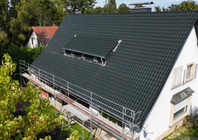 Vue a&eacute;rienne d'une grande toiture neuve en tuiles anthracite avec fen&ecirc;tre de toit, sur une maison blanche entour&eacute;e de verdure