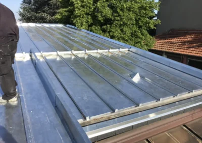 Zingueur travaillant sur une toiture en zinc &agrave; joint debout, arbres et b&acirc;timents en arri&egrave;re-plan